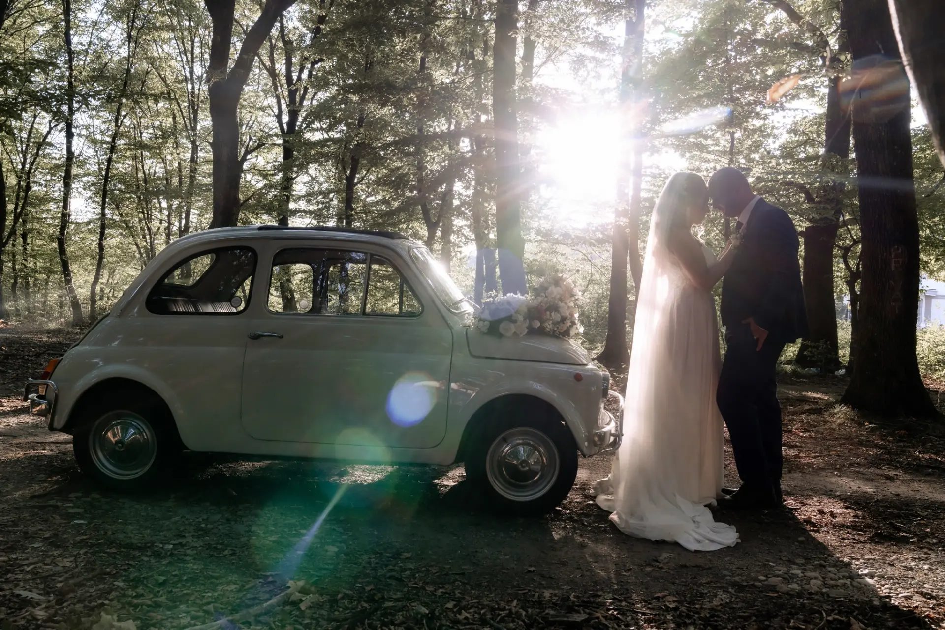 Miri lângă un Fiat 500 alb, în pădure, la apus